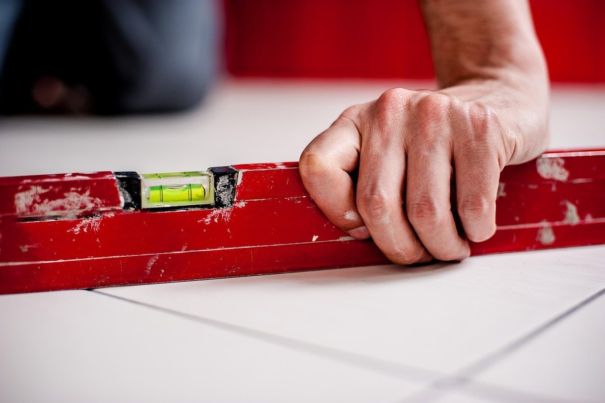 Un main appuie sur un niveau à bulle rouge posé sur carrelage blanc