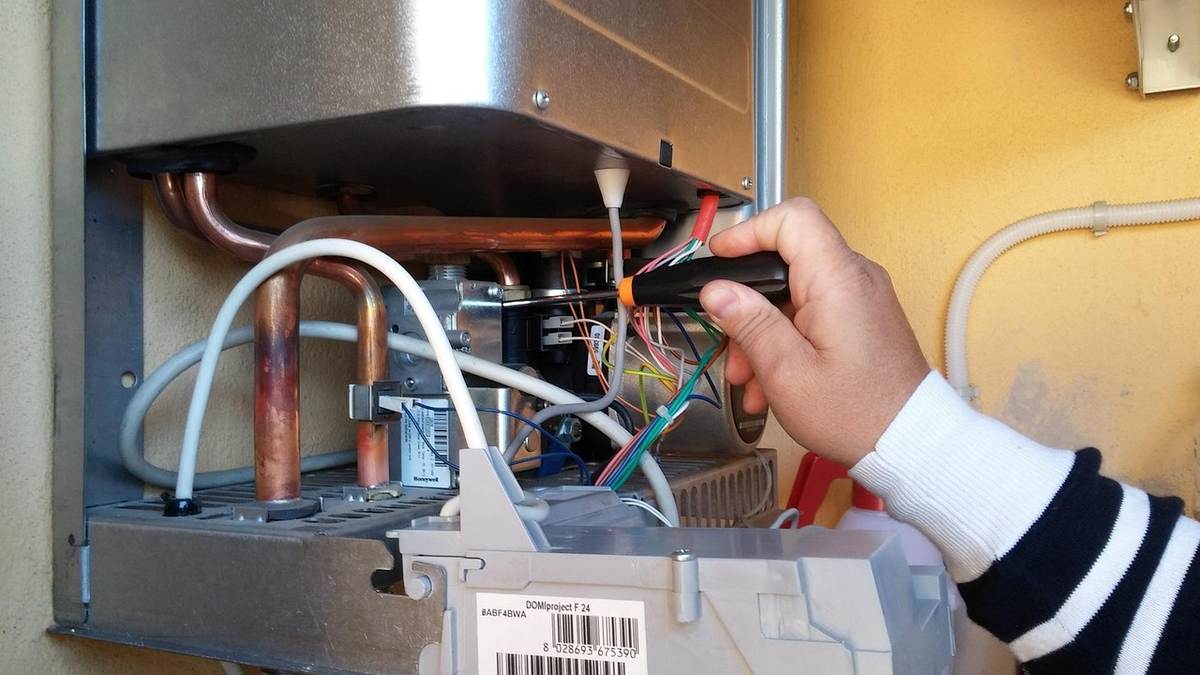Main à l'intérieur d'un appareil chauffant manipulant des câbles électriques