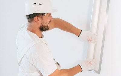 Un ouvrier en tenue blanche fixe un panneau sur un mur blanc