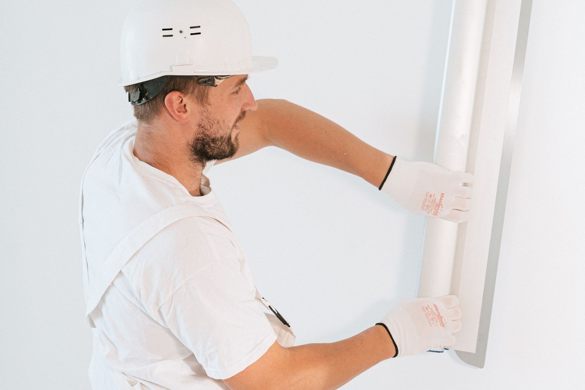 Un ouvrier en tenue blanche fixe un panneau sur un mur blanc