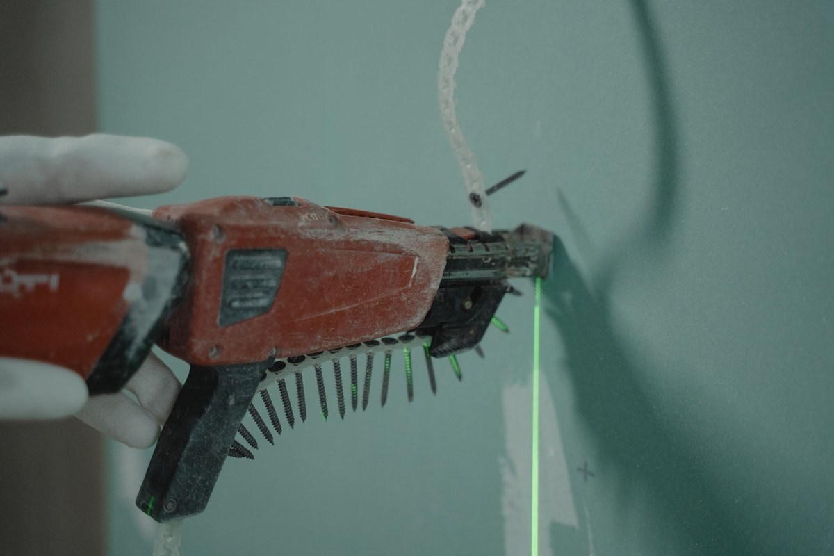 Une main gantée tient une perceuse à clous sur un mur avec laser vert Une main gantée tient une perceuse à clous sur un mur avec laser vert